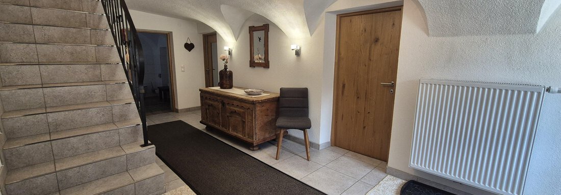 An inviting hallway with a staircase and a wooden dresser. The walls are painted in neutral colors and there is a cozy atmosphere. - Landhaus Waldesruh - Haiming