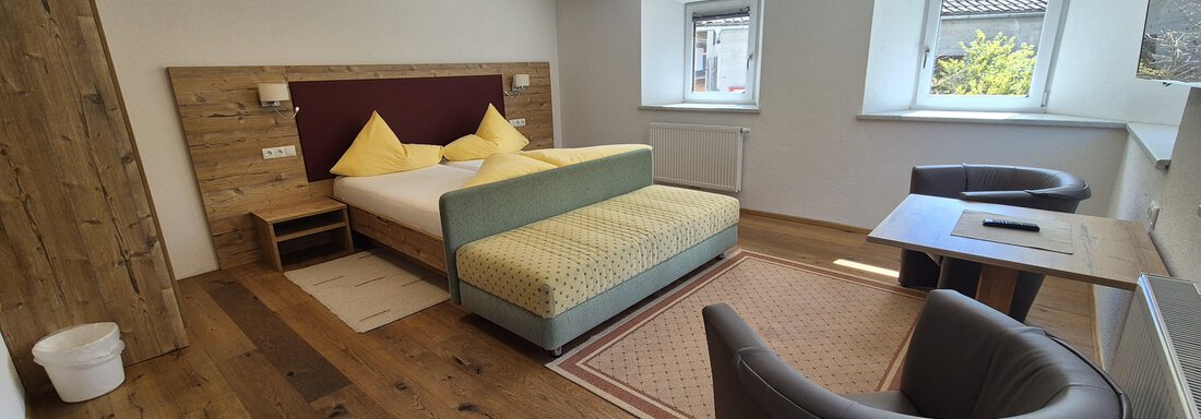 A modern room with a double bed and two comfortable armchairs.  
Bright colors and hardwood flooring create a cozy atmosphere. - Landhaus Waldesruh - Haiming