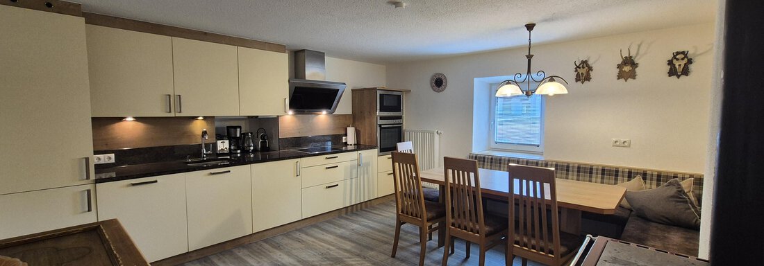 A modern kitchen with bright furniture and a dining area.  
Large kitchen island and windows provide plenty of light. - Landhaus Waldesruh - Haiming