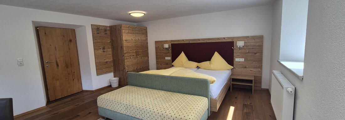 A modern bedroom with a large bed and bright walls. The wooden floor and furniture give the room a warm atmosphere. - Landhaus Waldesruh - Haiming