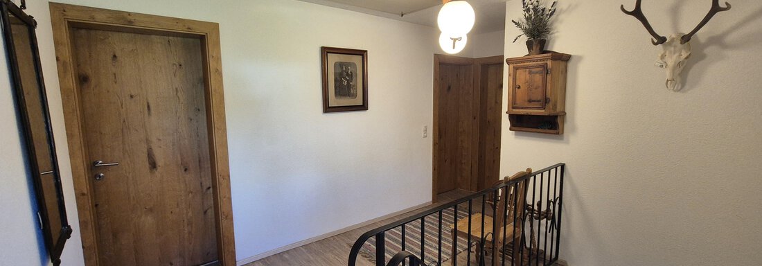 An inviting hallway with wooden doors and a rustic design.  
On the wall, there are some decorative elements such as an antler and a plant holder. - Landhaus Waldesruh - Haiming