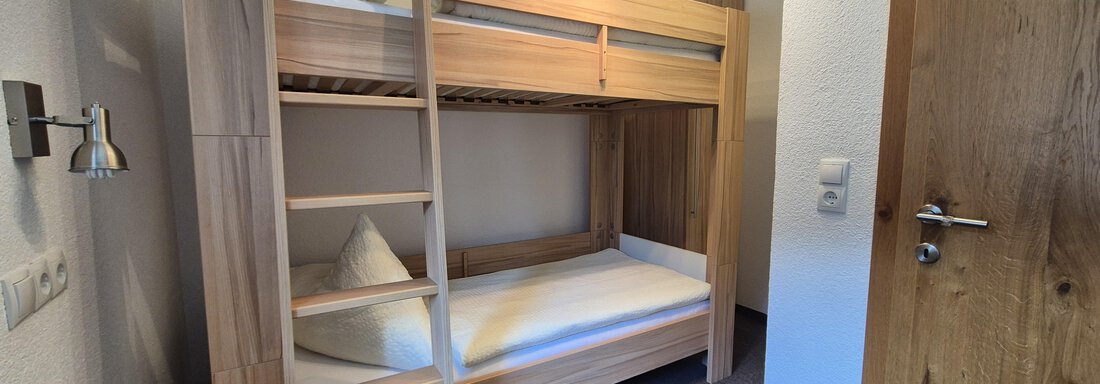 A room with a wooden bunk bed and a single bed. The walls are bright and the room feels cozy and tidy. - Landhaus Waldesruh - Haiming