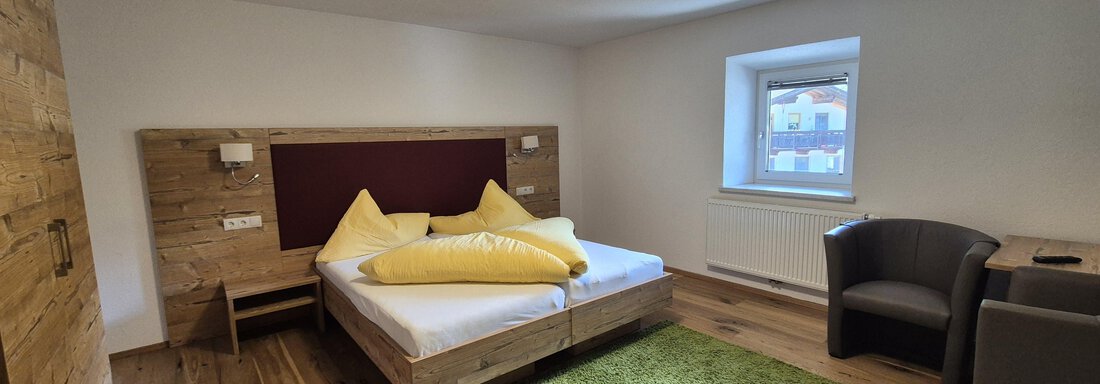 A modern bedroom with wooden elements and a comfortable bed. The room features a green carpet and two seating options. - Landhaus Waldesruh - Haiming