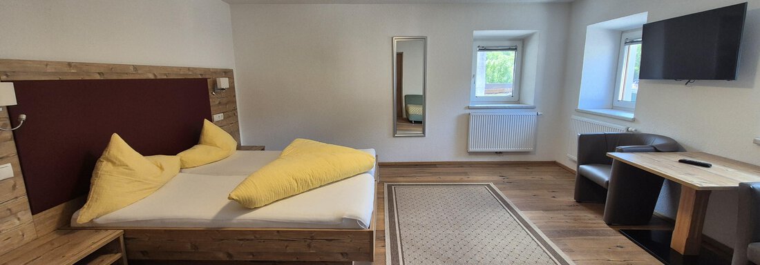 A cozy room with a double bed and wooden furniture. There is a television and a table with chairs. - Landhaus Waldesruh - Haiming