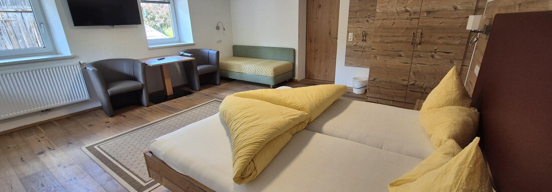 A cozy bedroom with a double bed and yellow pillows. The room features modern furniture, a television, and warm wooden design. - Landhaus Waldesruh - Haiming