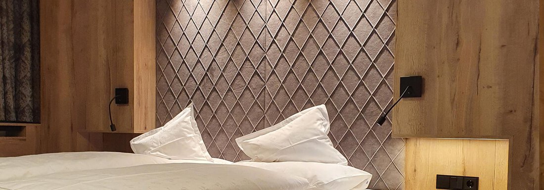 Doppelzimmer Kirchenkogel de Luxe - Laurin 2150 | © Alpenhotel Laurin (CC C) A modern bedroom with a large bed and a stylish wall covering. The warm wood tones and subtle lighting create a cozy atmosphere. - Alpenhotel Laurin - Hochgurgl