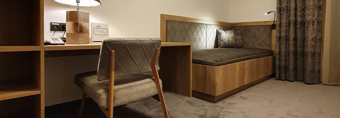 A modern room with a desk, a chair, and a cozy seating nook. The warm wood and gray colors create an inviting atmosphere. - Alpenhotel Laurin - Hochgurgl