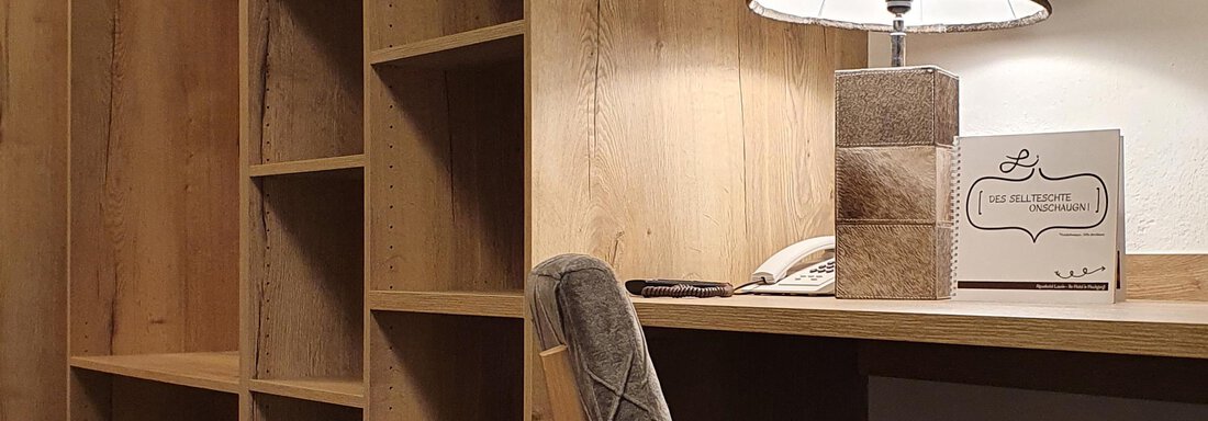 A modern room with wooden shelves and a desk. On the table, there is an elegant lamp and a call station. - Alpenhotel Laurin - Hochgurgl