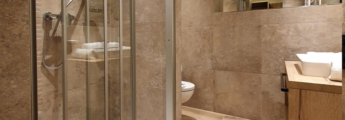 A modern bathroom with a glass shower and wooden details. The walls are in neutral earth tones. - Alpenhotel Laurin - Hochgurgl