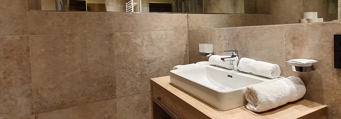 A modern bathroom with a wooden sink and a large mirror. The walls are painted in a light, neutral color. - Alpenhotel Laurin - Hochgurgl