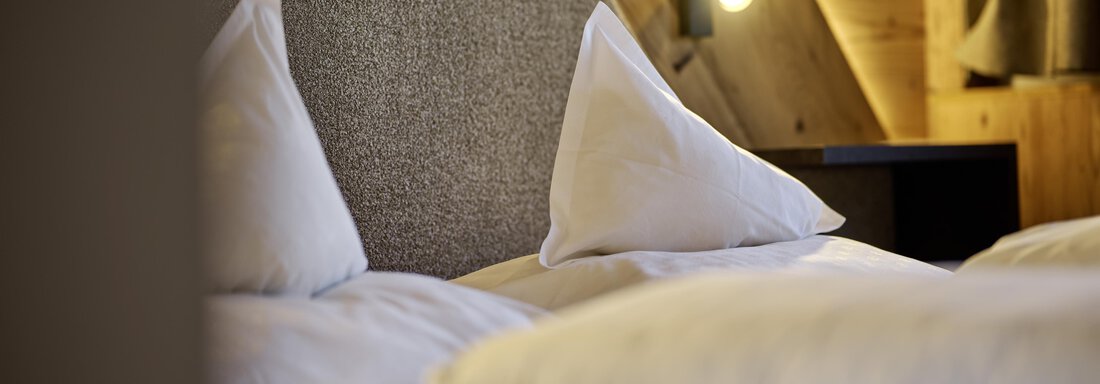 A cozy bedroom with white pillows and modern wood design. Soft light creates a relaxing atmosphere. - Alpenhotel Laurin - Hochgurgl