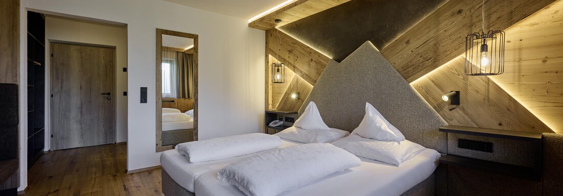 A modern bedroom with a large double bed and wooden paneling. The soft lighting creates a cozy atmosphere. - Alpenhotel Laurin - Hochgurgl