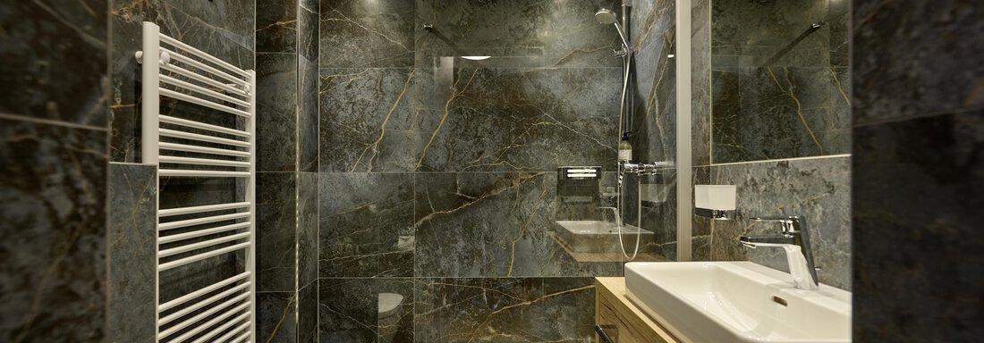 A modern bathroom with elegant gray tiles and a large shower. The furnishings include a sink and a towel warmer. - Alpenhotel Laurin - Hochgurgl