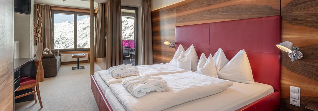 web-angerer-alm-zimmer-217--6 A modern hotel room with a large, comfortable bed and elegant wooden details. There is a window with a view of the mountains and a cozy seating area. - Hotel Angerer Alm - Hochgurgl