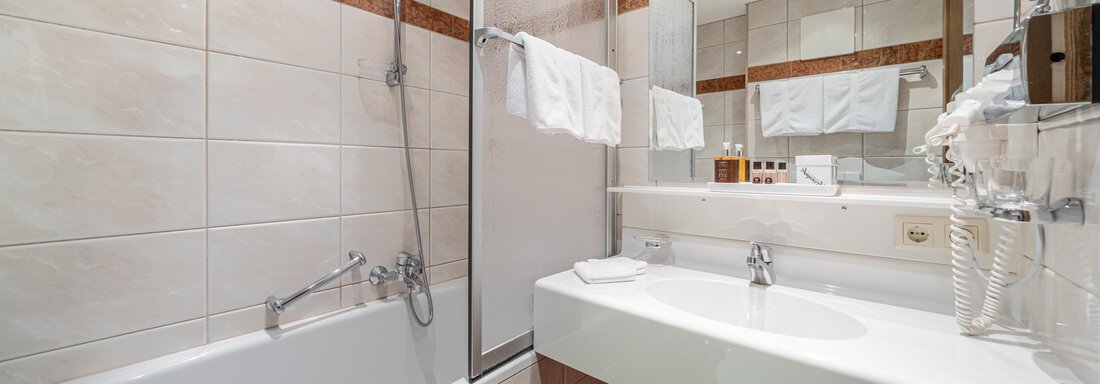 A modern bathroom with a bathtub and a shower. The walls are light-tiled and the space feels clean and inviting. - Hotel Angerer Alm - Hochgurgl