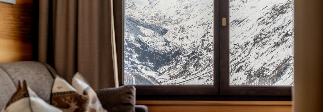 A cozy living room with a view of snow-covered mountains. The room is furnished with a sofa and a small table. - Hotel Angerer Alm - Hochgurgl