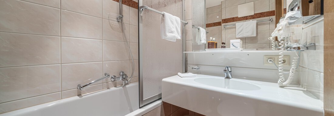A modern bathroom with a bathtub and a shower. It has bright tiles and an elegant sink. - Hotel Angerer Alm - Hochgurgl