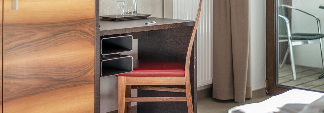 A modern desk with a chair in a bright room. In the background, a radiator and a window are visible. - Hotel Angerer Alm - Hochgurgl