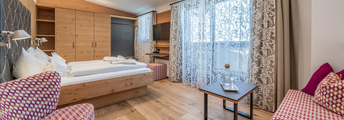 web-angerer-alm-zimmer446- A modern room with wooden flooring and a large window. The seating area is cozy and stylishly decorated. - Hotel Angerer Alm - Hochgurgl