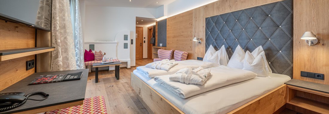 A modern hotel room with a large double bed and wood-paneled walls. The decor is bright and inviting, with a cozy seating area. - Hotel Angerer Alm - Hochgurgl
