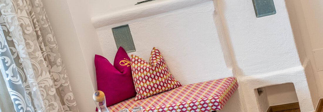 A cozy seating area with colorful cushions and a table. In the background, there is a stylish fireplace. - Hotel Angerer Alm - Hochgurgl