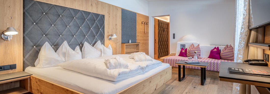 A modern hotel room with a large bed and elegant wood paneling. The room is bright and friendly, with a cozy seating area. - Hotel Angerer Alm - Hochgurgl