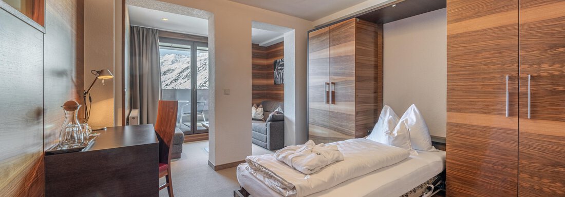 A modern bedroom with a single bed and wooden wardrobes. The room has large windows and a bright, welcoming style. - Hotel Angerer Alm - Hochgurgl