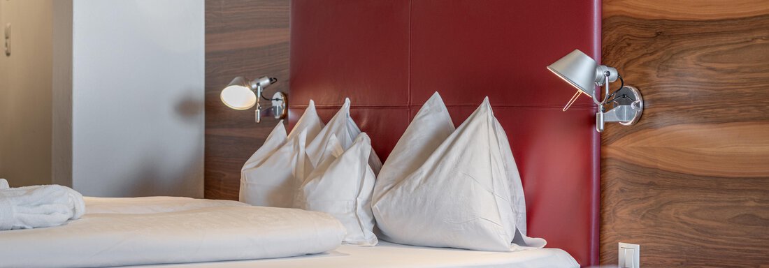 A comfortable hotel room with two beds and red headboards. The bedding is well-kept and there are bedside lamps. - Hotel Angerer Alm - Hochgurgl