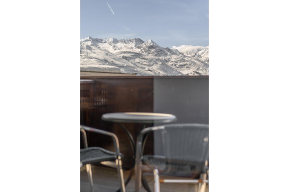A table and chairs with a view of snow-covered mountains. The sky is clear and blue. - Hotel Angerer Alm - Hochgurgl