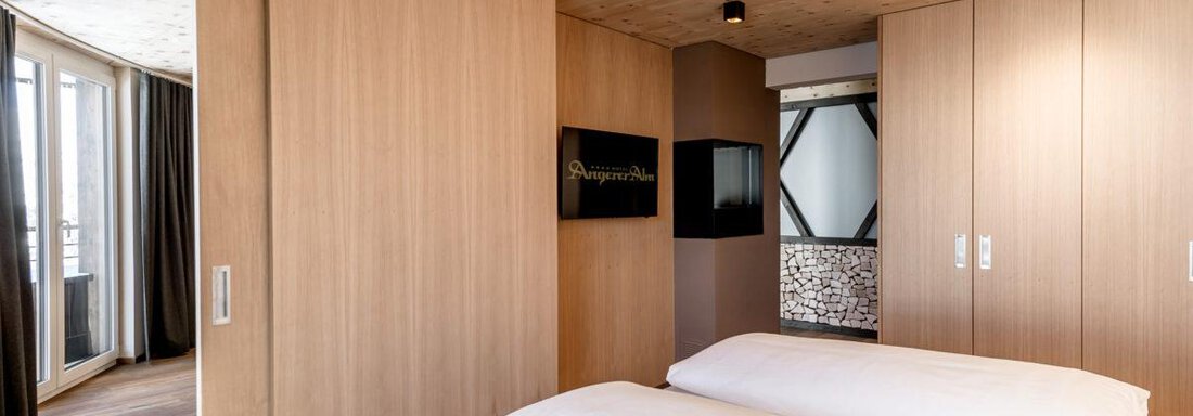 A modern bedroom with wooden paneling and two beds. Large windows provide plenty of light and a pleasant atmosphere. - Hotel Angerer Alm - Hochgurgl