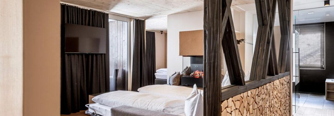 A modern room with a cozy sleeping area and a separate living area. The interior is stylishly designed with wood and neutral colors. - Hotel Angerer Alm - Hochgurgl