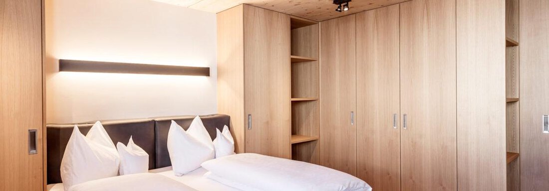 A modern bedroom with a double bed and elegant wooden furniture. The walls are light and there is plenty of storage space. - Hotel Angerer Alm - Hochgurgl