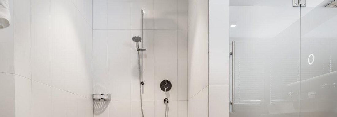 A modern shower in a bright bathroom. The walls are lined with white tiles and the shower is separated by a glass door. - Hotel Angerer Alm - Hochgurgl