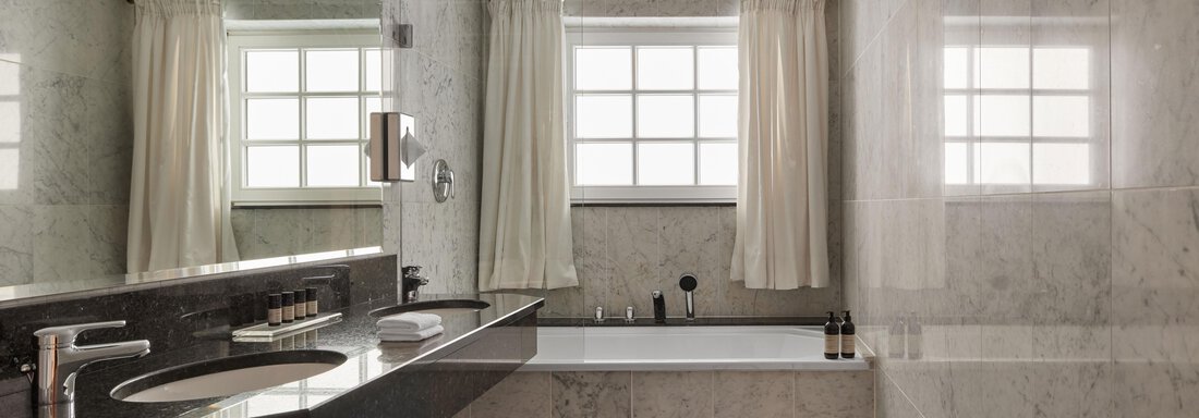 Ein modernes Badezimmer mit marmorierten Wänden und einer Badewanne. Große Fenster lassen viel Licht herein und sorgen für eine helle Atmosphäre. - TOP Hotel Hochgurgl - Hochgurgl