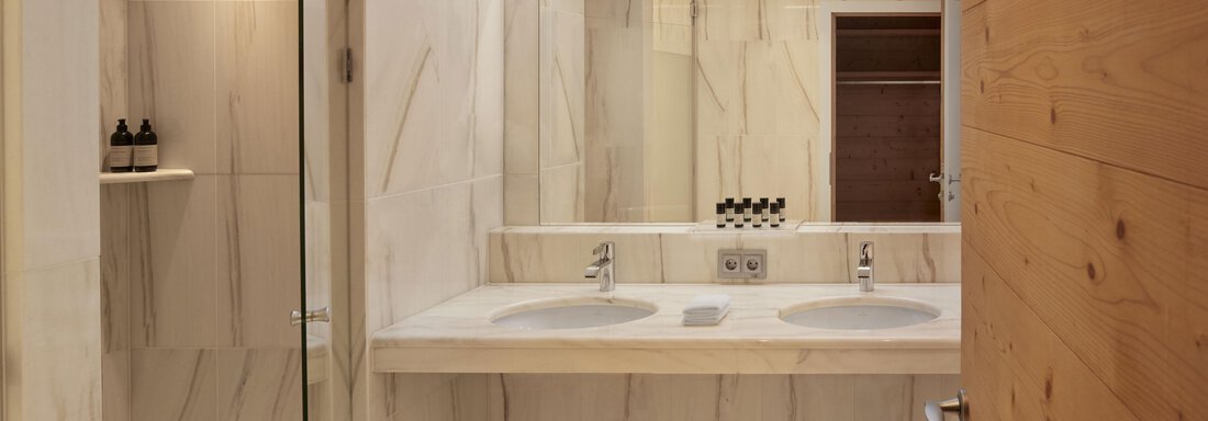 Ein modernes Badezimmer mit hellen Marmorwänden und zwei Waschbecken. Die Beleuchtung sorgt für eine angenehme Atmosphäre. - TOP Hotel Hochgurgl - Hochgurgl