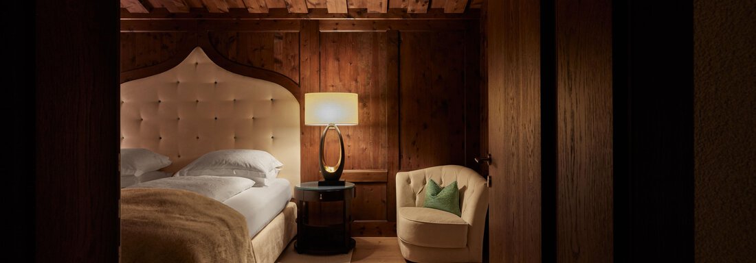 Junior Suite Ein gemütliches Schlafzimmer mit einem großen, gepolsterten Bett und einem hellen Sessel. Die Wände sind aus Holz, was eine warme Atmosphäre schafft. - TOP Hotel Hochgurgl - Hochgurgl