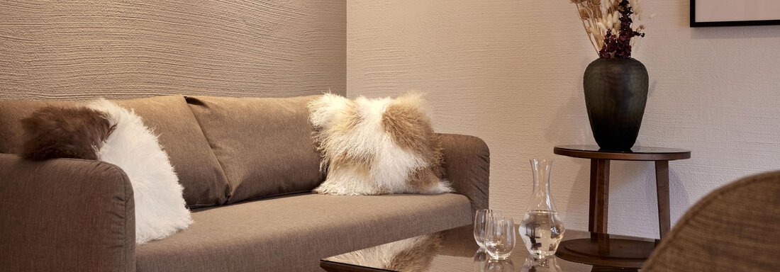 Ein gemütliches Wohnzimmer mit einem beigen Sofa und dekorativen Kissen. Neben einem Glastisch steht ein schwarzes Gefäß mit Trockenblumen. - TOP Hotel Hochgurgl - Hochgurgl