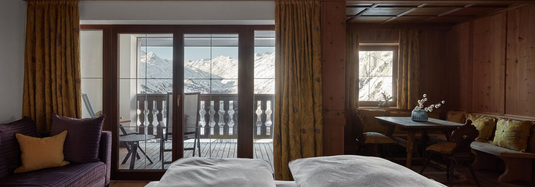 Ein gemütliches Zimmer mit Holzverkleidung und großen Fenstern. Der Blick geht auf die Berge und einen Balkon. - TOP Hotel Hochgurgl - Hochgurgl
