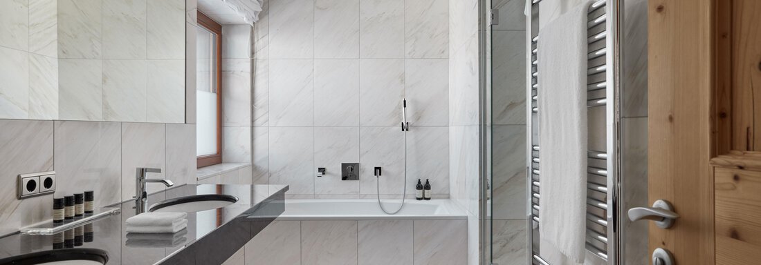 Ein modernes Badezimmer mit hellen Fliesen und eleganten Armaturen. Es verfügt über eine Badewanne, zwei Waschbecken und eine große Dusche. - TOP Hotel Hochgurgl - Hochgurgl