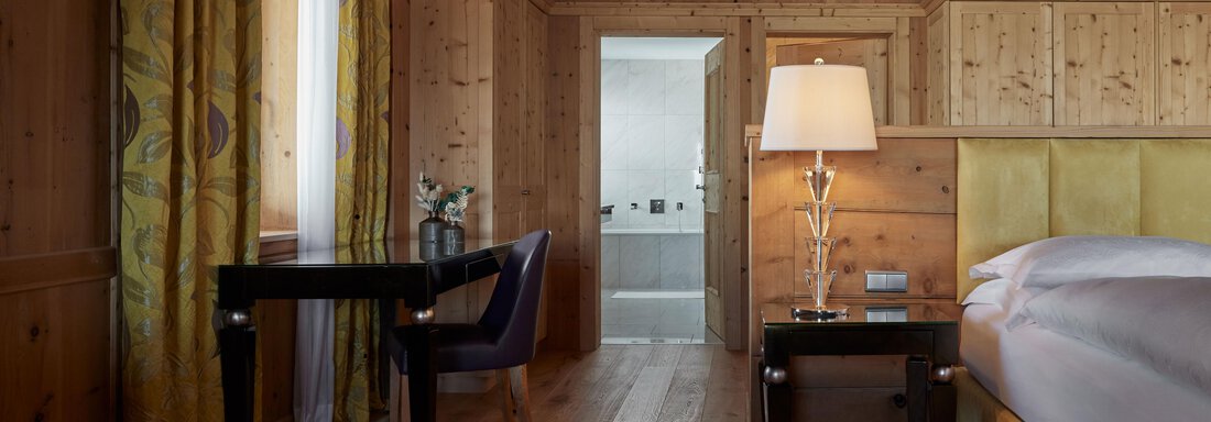 Ein stilvolles Zimmer mit Holzverkleidungen und einem gemütlichen Bett. Ein kleiner Schreibtisch mit einem Stuhl und sanftem Licht aus einer Lampe. - TOP Hotel Hochgurgl - Hochgurgl