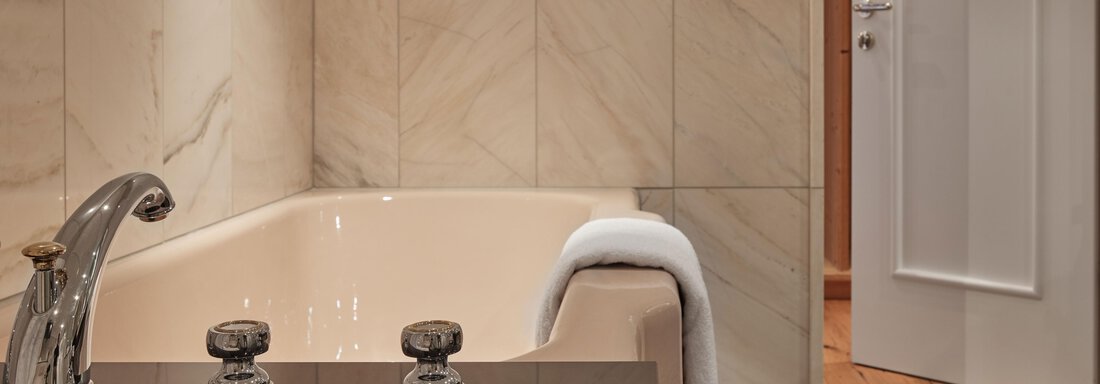 Ein elegantes Badezimmer mit einer modernen Badewanne und stilvollen Armaturen. Die Wände sind mit schickem Marmor verkleidet, und eine Tür führt zu einem weiteren Raum. - TOP Hotel Hochgurgl - Hochgurgl