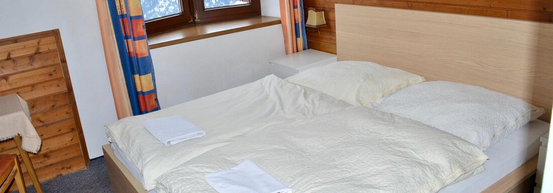 A cozy bedroom with a double bed and two windows. The walls are made of wood, and the decoration is simple, with a clear view outside. - Haus Maria - Hochsölden