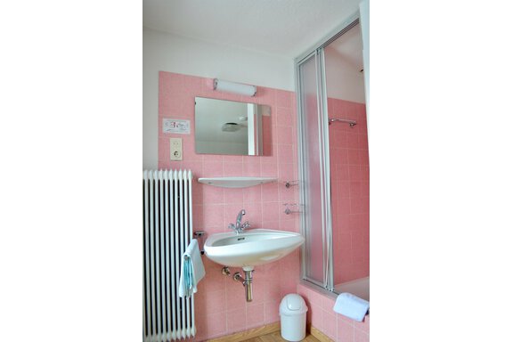 A modern bathroom with pink tiles and a shower cubicle. There is a sink, a mirror, and a heating system. - Haus Maria - Hochsölden