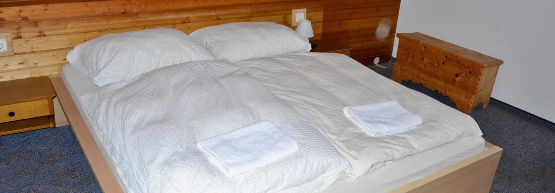 A cozy bedroom with a double bed and wood paneling. There are fresh towels on the bed and a wooden wardrobe in the corner. - Haus Maria - Hochsölden