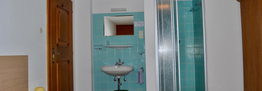 A simple bedroom with a bed, a sink, and a shower. The walls are light and the furnishings are functional. - Haus Maria - Hochsölden