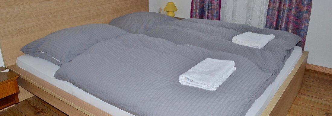 A cozy bedroom with a double bed and light pillows. The wooden floor and the windows create a warm atmosphere. - Haus Maria - Hochsölden