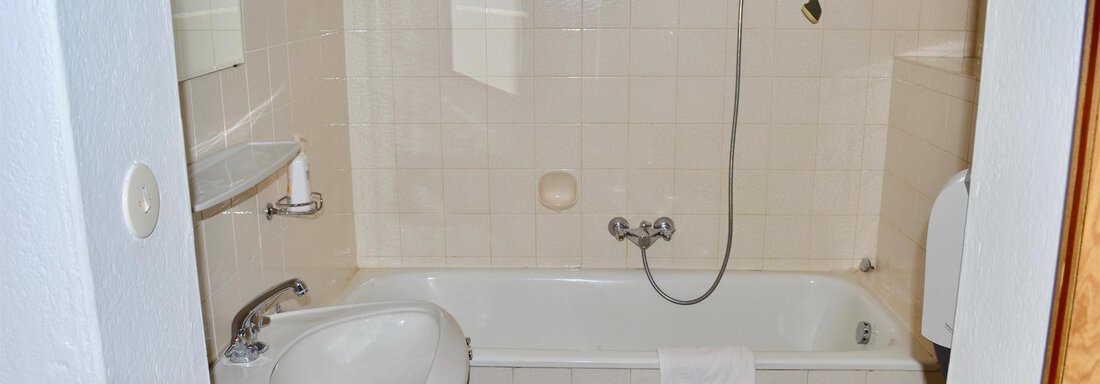 A simple bathroom with a bathtub and a sink. The walls are tiled in light colors and there is a showerhead. - Haus Maria - Hochsölden