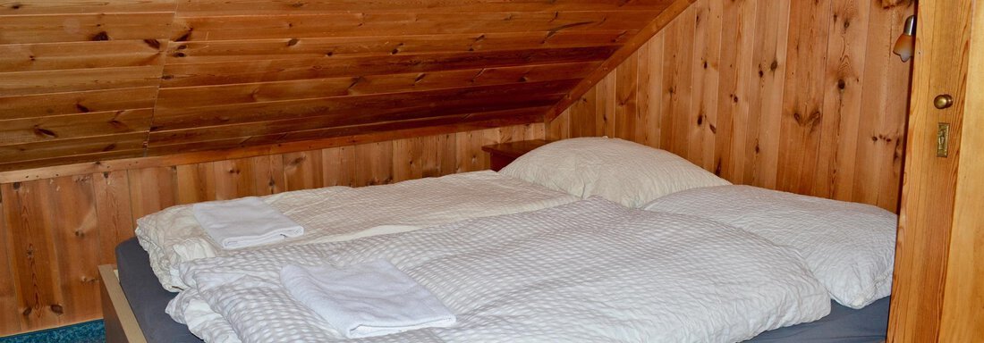 A cozy attic bedroom with a double bed and wood paneling. The bedding is tidy and there are fresh towels. - Haus Maria - Hochsölden
