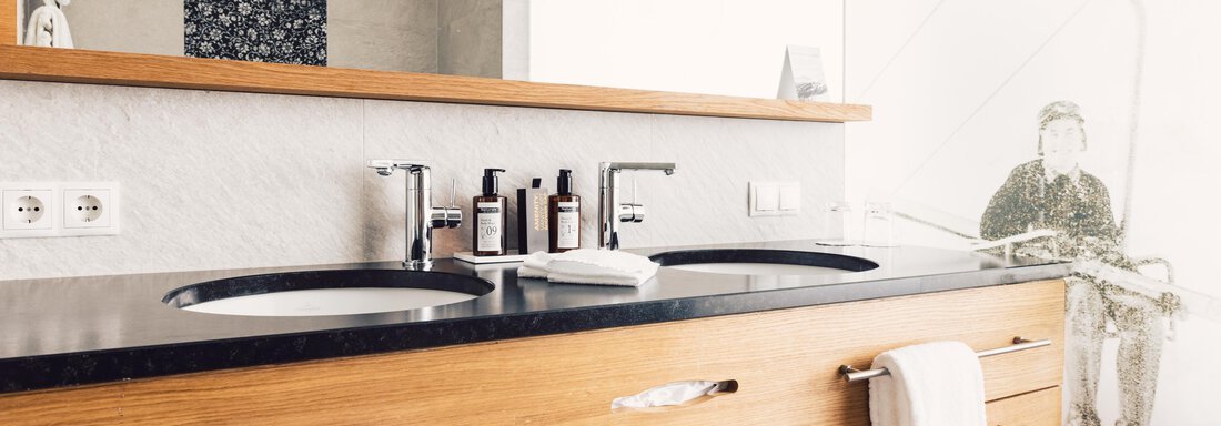 A modern bathroom with two sinks and a wooden dresser. The walls are elegantly designed and an interesting wall painting is visible. - 4 * Superior Hotel Schöne Aussicht - Hochsölden