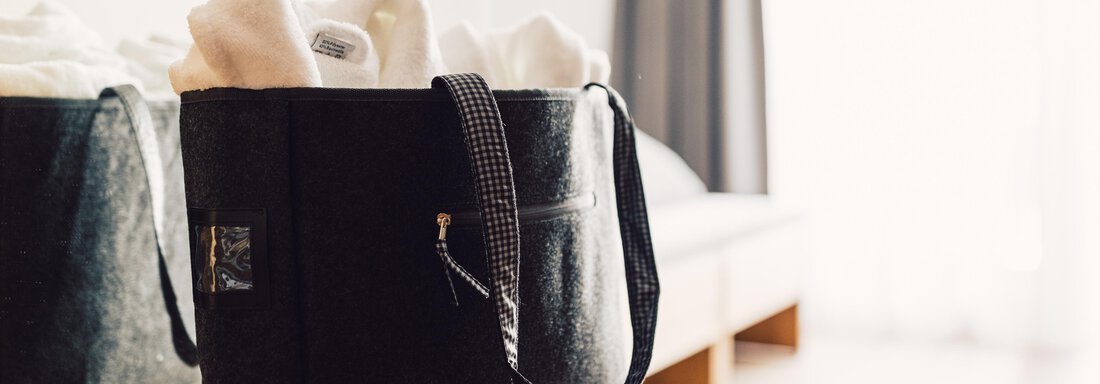 A stylish black bag stands on a wooden shelf. It contains several white towels and is placed against a bright background. - 4 * Superior Hotel Schöne Aussicht - Hochsölden